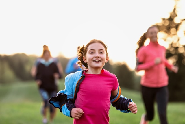 Child running and smiling, with other children and adults running in the background